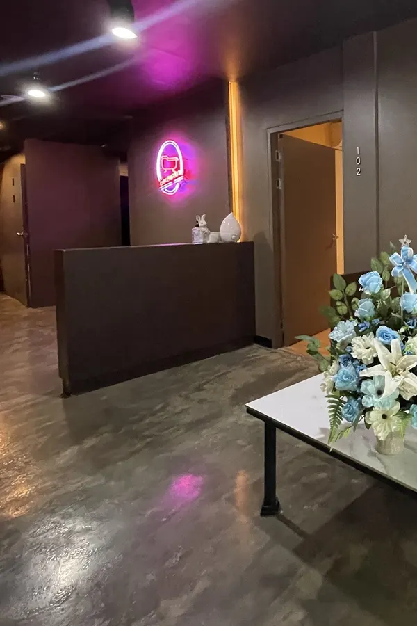 The reception desk with a pink neon logo, and a table with a bouquet of blue and white flowers