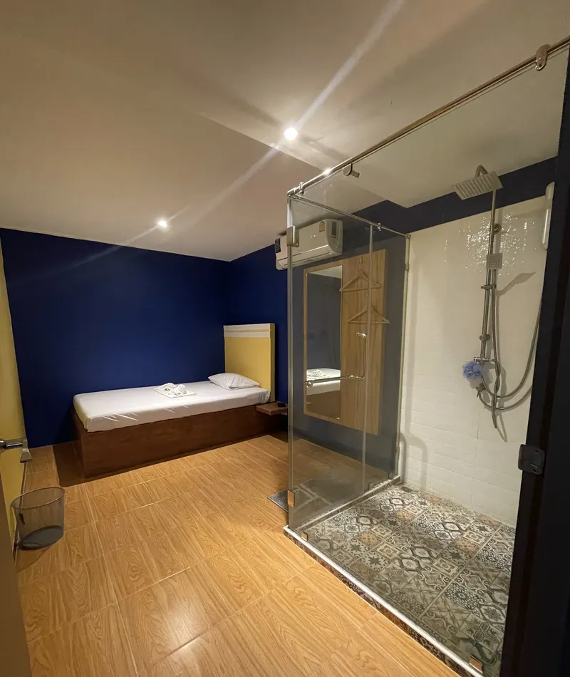 Shower room with a glass walk-in shower and a single bed against blue walls